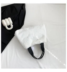Close-up of white plush bucket bag featuring black strap and soft faux fur pom-pom detail