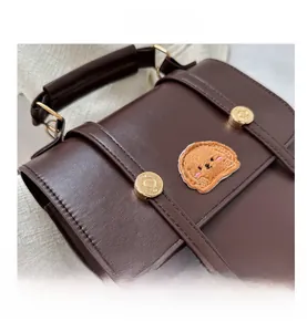 Close-up of deep brown PU leather bag featuring cute puppy embroidery and gold metal buckles
