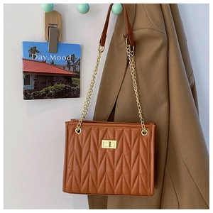 Detail of brown quilted bag with V-shaped texture, gold chain strap and metal lock closure