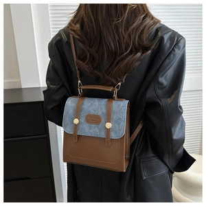 Détail du sac à dos en denim bleu et cuir marron porté par un mannequin en cuir noir