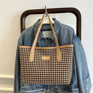 Large houndstooth tote bag with brown leather handles on a blue denim jacket background