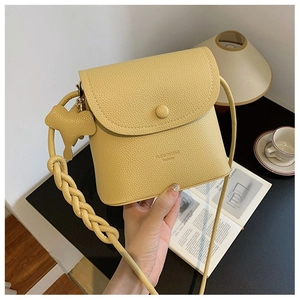 Detail of yellow lychee texture bag with woven strap and elephant charm in a lifestyle set