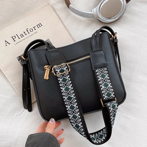 Chic black crossbody bag with wide geometric woven strap and gold hardware on fabric