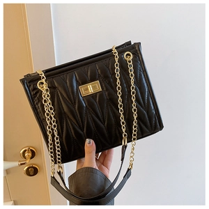 Detail of a black quilted shoulder bag with a gold chain strap and turn-lock closure