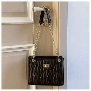 Close-up of black quilted leather shoulder bag with gold chain and metal twist lock