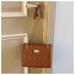 Detail of caramel brown quilted shoulder bag with V-shaped stitching and gold twist lock