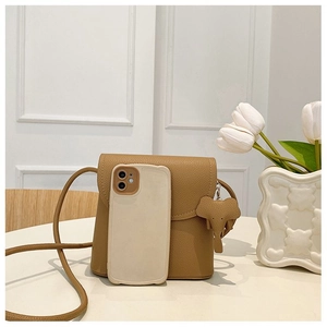 Mini khaki pebble leather crossbody bag with elephant charm next to a smartphone