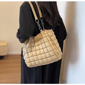 Detail of beige quilted puffer tote bag with metal chain strap worn by a model