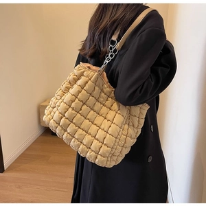 Close-up of beige quilted tote bag with chain strap and bubble texture on a model