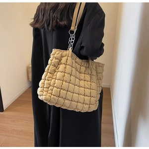 Detail of khaki quilted tote bag featuring padded square texture and silver chain strap