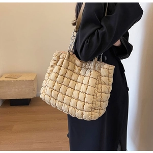 Detailed side view of beige quilted tote bag with metal chain and leather strap