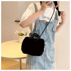 Detail of black faux fur plush handbag with woven handles and leather strap on model