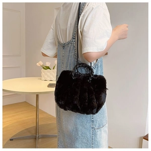 Detail of black fluffy faux fur handbag with a twisted handle and slender leather strap