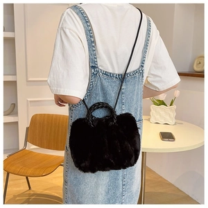Detail of a black plush handbag with woven handles and a slim crossbody shoulder strap