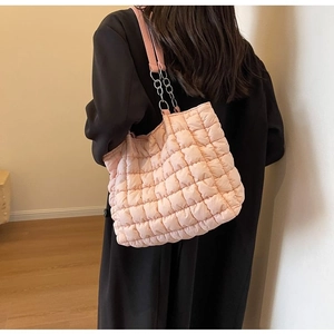 Pink quilted cloud tote bag with chain strap shown on a model in a black coat