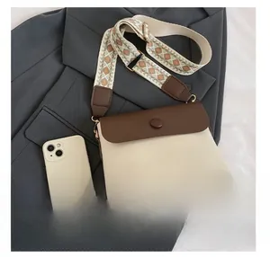 Détail du sac à bandoulière rétro bicolore avec sangle large à côté d'un smartphone