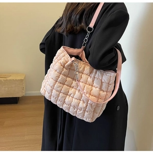 Detail of pink quilted puff shoulder bag with metal chain strap on model in black coat