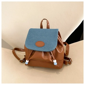Detalle de mini mochila vaquera con piel sintética marrón y pompones de cordón