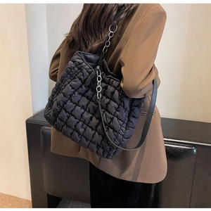 Detail of a large black quilted tote bag with silver chain strap on a model's shoulder