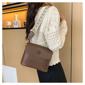 Sac bandoulière en cuir marron avec large sangle ethnique porté sur un pull blanc