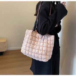 Pink quilted puffer tote bag with silver chain strap shown on a model in a modern room