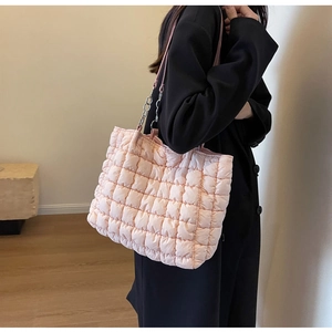 Close-up of a pink quilted tote bag with chain strap held by a model in casual attire