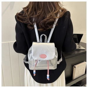 Détail d'un mini sac à dos argenté métallisé avec cordon rose et étiquette logo tendance