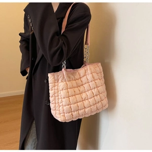 Detailed shot of pink quilted tote bag with silver chain strap on black coat
