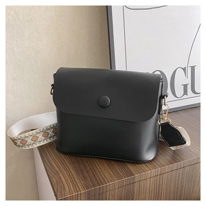 Détail d'un sac bandoulière noir avec sangle large à motifs et ferrures dorées