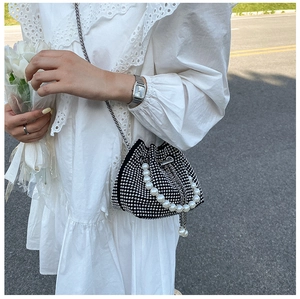 Dettaglio di una borsa a secchiello nera con strass, manico di perle e catena su abito bianco