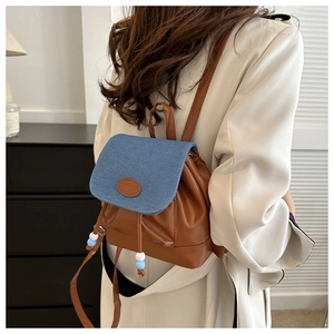 Détail du mini sac à dos montrant le rabat en denim, logo FASHION et cordon de serrage