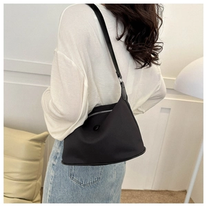 Minimalist black nylon crescent bag shown worn on a model's shoulder in a home setting