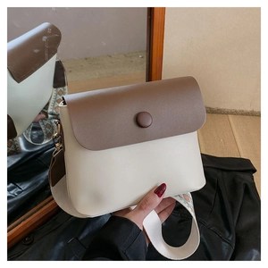 Gros plan d'un sac bandoulière bicolore avec une large bandoulière en tissu tressé