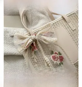 Detail of straw tote bag featuring white lace bow and pink rose floral embroidery decoration