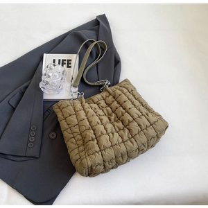 Detail of olive green quilted puffer tote bag with metal chain strap on a gray suit