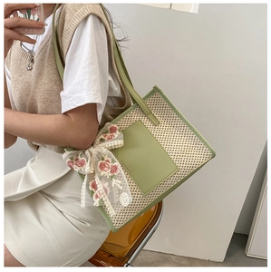Straw tote bag detail with green leather trim and floral lace bow on a model