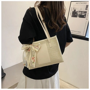 Close-up of beige straw beach bag featuring a red floral lace bow and leather patch