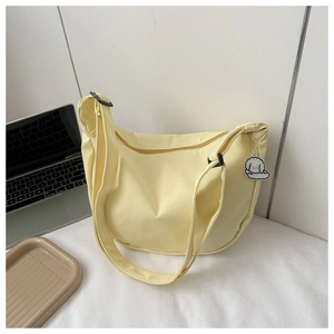 Close-up of a yellow waffle canvas crescent bag with a cute poodle charm on a bed