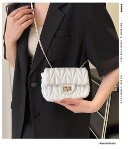 White quilted crossbody bag with gold chain strap shown on model in black blazer