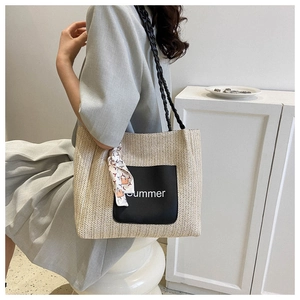 Detail of woven straw tote bag featuring Summer lettering and silk scarf on black handle