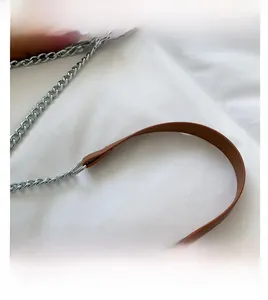 Detail view of brown leather shoulder strap with silver metal chain on a white background