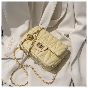 Detail of cream quilted bag featuring a gold twist lock and a chain strap with a gold ball