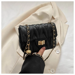 Detail of black quilted shoulder bag with gold chain strap and spherical charm on a blazer