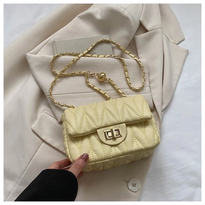 Detail of beige quilted crossbody bag with golden chain strap and adjustable gold ball