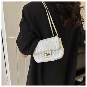 Detail of white V-quilted chain bag with gold twist lock worn over a black blazer