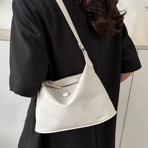 White nylon hobo shoulder bag with zipper and round buckle worn over a black blazer