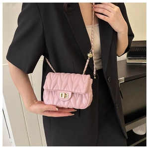 Detail of pink quilted leather crossbody bag with gold chain strap on a model wearing black