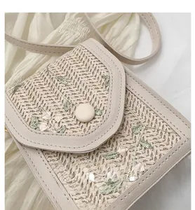 Detailed view of beige woven crossbody bag featuring floral embroidery and leather trim