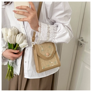 Detail of woven straw cell phone bag featuring floral embroidery and adjustable leather strap