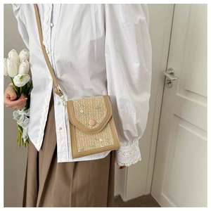 Close-up of woven straw crossbody bag with floral embroidery and brown leather trim
